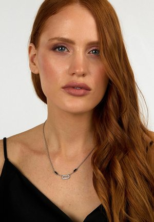 Collana d'argento con un link testurizzato e accenti neri; indossata sulla pelle nuda, presenta un design contemporaneo e una catena fine.