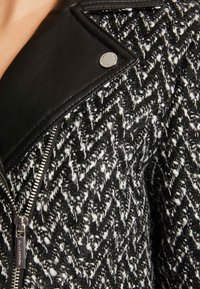 Svart och vit herringbone-mönstrad tygjacka med läderkrage, silverblixtlås och metallaccentdetaljer. Texturerad med ett vävt utseende.