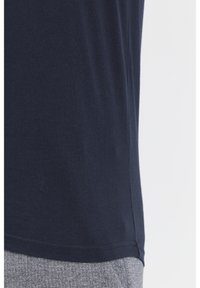 Navyblaues Baumwoll-T-Shirt mit kurzen Ärmeln, glatter Textur, seitlichem Schlitzdetail und abgerundetem Saum. Kombiniert mit grauen gemusterten Hosen.