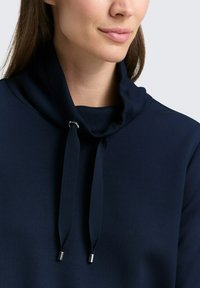 Marineblauer Kapuzenpullover mit hohem Kragen, Kordeln und Metallstoppern. Glatte Textur, minimalistisches Design ohne Muster oder Verzierungen.