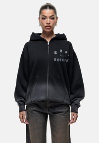 Felpa nera con zip, dal fit morbido, dotata di tasca frontale e design con testo stampato. Realizzata in tessuto morbido con bordi leggermente sbiaditi.