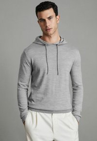 Grau gepulllter Hoodie aus weichem Stoff, mit einer Kordel, langen Ärmeln und gerippten Bündchen. Kombiniert mit hellen Hosen.