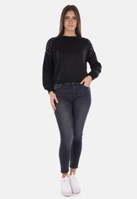 Felpa nera con spalline decorate, abbinata a jeans scuri e sneakers bianche. Il tessuto è morbido e il design è casual.