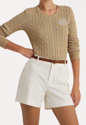 Beige kabelgebreide trui met ronde hals en decoratieve knopen, gecombineerd met witte op maat gemaakte shorts en een bruine leren riem.