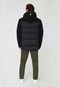 Svart puffjacka med huva, med kviltad textur och släta ärmar. Matchad med olivgröna byxor och vita sneakers.