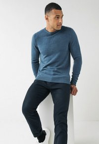Suéter azul con cuello redondo y mangas largas, combinado con pantalones oscuros y zapatillas blancas. La tela parece suave con una textura lisa.