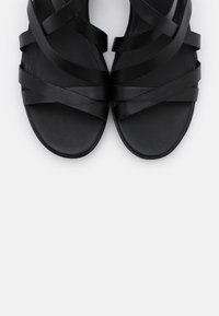 Černé sandály s vícero křížícími se popruhy vyrobené z hladké kůže, s plochou podrážkou a zakulacenou špičkou. Jednoduchý, minimalistický design.