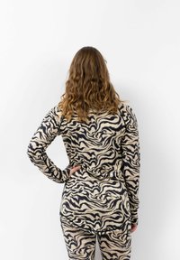 Langsleeve top en leggings in een beige en zwart draaiend patroon. Zacht, rekbaar materiaal met een ontspannen pasvorm en afgeronde zoomafwerking.