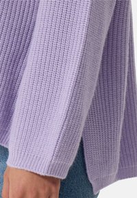 Pull en laine lavande avec une texture en côtes, présentant des manches longues et une coupe décontractée avec des motifs de tricot visibles et des poignets côtelés.