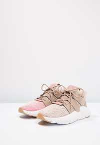 Beżowe i różowe trampki z teksturowaną cholewką z dzianiny, okrągłym noskiem i białą gumową podeszwą. Zawierają sznurowadła oraz dwukolorowy design.