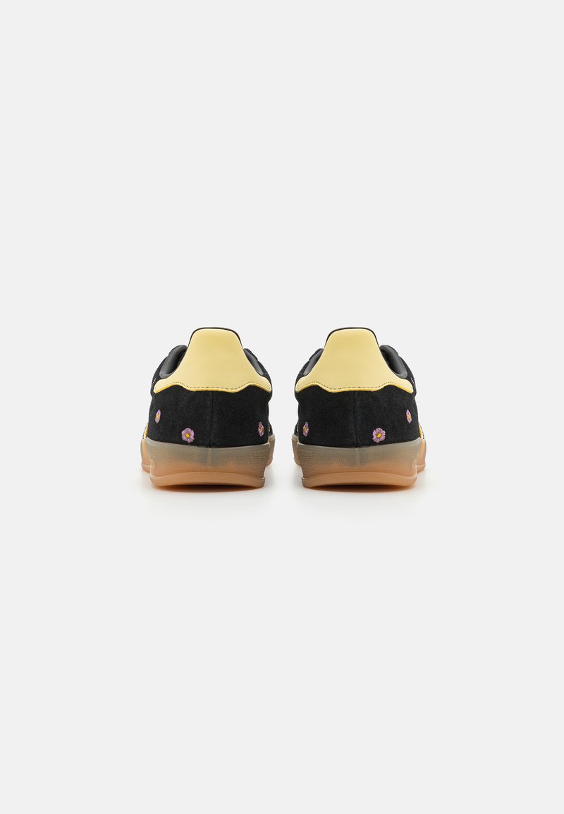 Sneakers in suede nero con dettagli gialli, caratterizzati da ricami floreali e una suola in gomma. Vista da dietro.