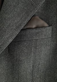 Grau meliertes Fischgrätgewebe mit maßgeschneidertem Design, sichtbarer Tasche und glattem Futterstoff.