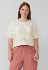 Crème-kleurig oversized t-shirt met een graphic van palmbomen en een zon. Gecombineerd met zachte, geplooide koraalkleurige broek.