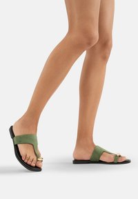 Sandales en daim vert avec un accent doré et une semelle en caoutchouc noir. Design ouvert à l'avant et profil plat pour un usage décontracté.