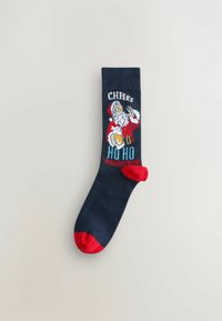 Marineblauer Socke mit roten Zehen- und Fersenakzenten. Mit einem Santa-Grafik, der ein Bier hält, sowie dem Text "CHEERS" und "HO HO HALT MEIN BIER" in Weiß und Blau.