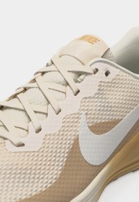 Baskets Nike beige et sable avec dessus texturé, logo Nike blanc en forme de virgule, et lacets assortis beige, vues en gros plan sous un angle oblique.