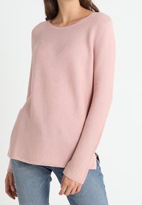 Light pink ribbed sweater with a round neckline and long sleeves, featuring side slits, paired with blue jeans.