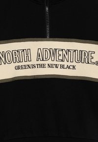 Sudadera con cremallera negra que presenta una banda crema con ribete verde, con el texto "NORTH ADVENTURE" y "GREEN IS THE NEW BLACK". Textura suave.
