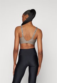 Grå sportsbra med justerbare stropper som har "Under Armour"-merke, paired med høyt liv svarte leggings, glatte tekstur.
