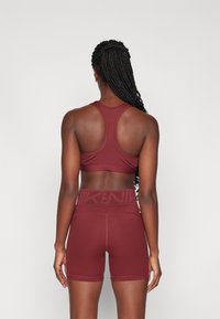 Bordo sportski grudnjak s dizajnom racerback i usklađenim visokim hlačicama, izrađen od glatkog, rastezljivog materijala s pojasom sa logotipom.
