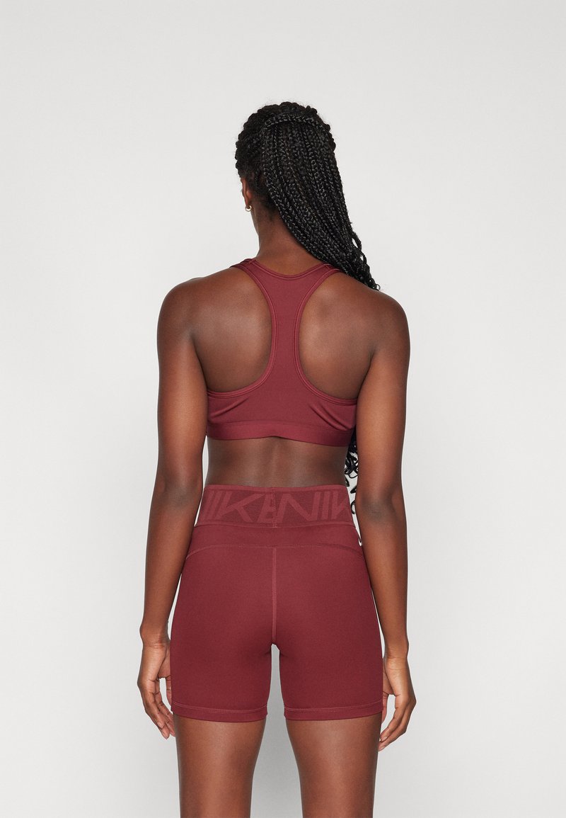 Reggiseno sportivo bordeaux con design a racerback e pantaloni corti a vita alta coordinati, realizzati in tessuto liscio e elasticizzato con vita decorata da logo.