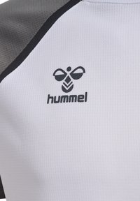 Witte sportt-shirt van een textuurstof, met grijze accenten op de mouwen. Zwart logo van een bij en de merknaam "hummel" prominent weergegeven.