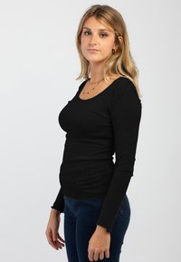 Maglietta nera a maniche lunghe con scollatura a girocollo. Design aderente, tessuto testurizzato, con bordi grezzi su maniche e orlo.