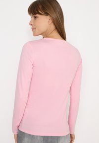 Langærmet top i lyserødt stof med rund halsudskæring og tætsiddende design. Glat tekstur med minimal dekoration.