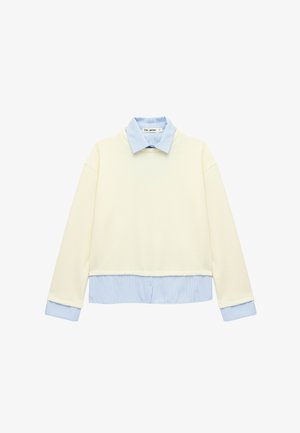Langærmet cremefarvet pullover lagdelt over en blå- og hværandig skjorte med krave og matchende manchetter og kantdetaljer.