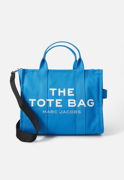 Borsa a spalla rettangolare blu brillante con manici corti, tracolla nera e la scritta bianca "THE TOTE BAG MARC JACOBS" sul fronte.