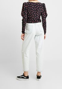 Top nero floreale a maniche lunghe con maniche arricciate, abbinato a jeans tapered chiari e sneaker nere con strisce bianche.