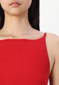 Débardeur rouge à côtes avec un encolure droite et des bretelles fines. Le tissu semble doux et texturé, mettant en valeur une conception ajustée.