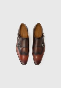 Zapatos de cuero marrón con un diseño elegante, que cuentan con una hebilla y perforaciones decorativas a lo largo del borde. Color degradado de marrón oscuro a claro.