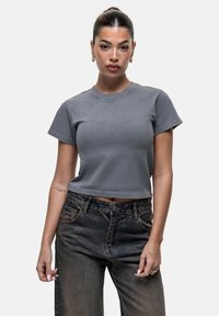 T-shirt grigia corta con maniche corte e scollo rotondo, realizzata in tessuto morbido; abbinata a jeans in denim scuro a vita alta.