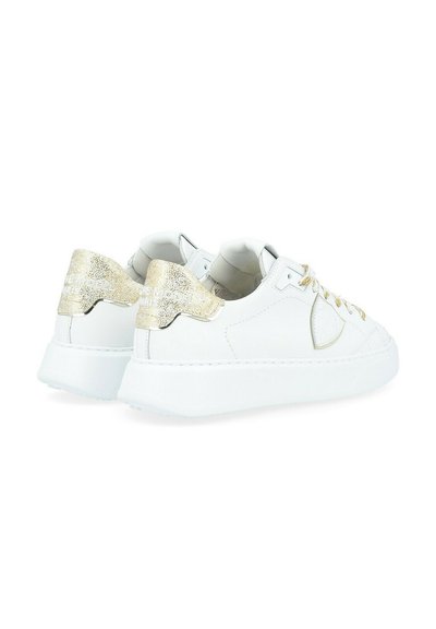 Des sneakers blanches en cuir avec un accent doré texturé sur le talon, dotées de lacets dorés et d'un design élégant et minimaliste. Semelle en caoutchouc.