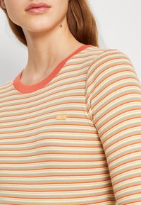 Gestreiftes Langarmhemd in Pastellfarben mit orangefarbener Rippkragen. Besitzt ein kleines gelbes Levi's-Logo auf der Brust. Weicher, strukturierter Stoff.