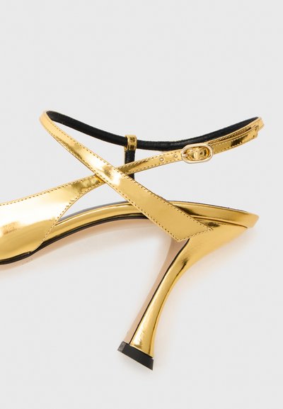 Sandale à talon haut en métal doré avec bout ouvert, brides entrecroisées et un talon effilé élégant avec un accent noir en dessous.