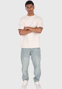 Lys beige bomull t-skjorte med korte ermer, kombinert med lyseblå jeans og hvite joggesko. Enkelt, avslappet snitt, ensfarget design.