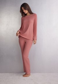 Roze longsleeve top en bijpassende broek van zachte stof. De top heeft een ronde halslijn en contrasterende afwerking; de broek heeft een rechte pijp ontwerp.
