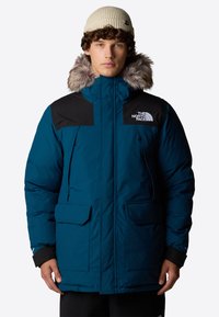 Teal isolerad jacka med svarta detaljer och en fluffig huva. Egenskaper: dragkedja och tryckknappar, två stora framfickor och logodetalj.