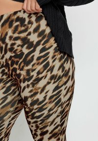 Leggings con stampa leopardata in beige e nero, caratterizzati da una texture liscia e una vestibilità slim, abbinati a un maglione nero lavorato a maglia in vita.