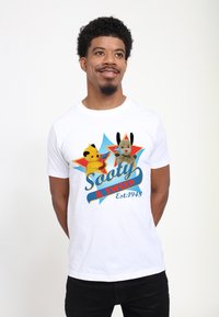 Bílý bavlněný tričko s barevným uměním dvou loutek, Sooty a Sweep, s textem v modré a červené barvě a pozadím ve tvaru trhající hvězdy.