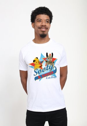 Hvid bomulds-t-shirt med farverigt kunstværk af to dukker, Sooty og Sweep, med tekst i blå og rød samt en stjerneeksplosionsbaggrund.