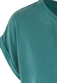 Chemise à manches courtes de couleur bleu sarcelle avec des revers roulés et un col en V, présentée sur un fond blanc uni.