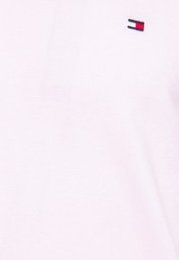 Jasnoróżowy sweter dzianinowy z małym, haftowanym logo w kolorach czerwonym, białym i niebieskim, o gładkiej teksturze i klasycznym kroju.