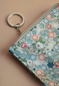Pouch s cvetličnim vzorcem v svetlo modrem materialu z srebrnim zadrgo in obročkom. Ima večbarvne rože in zelene poudarke na teksturiranem materialu.
