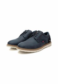 Zapatos sintéticos azul oscuro con textura suave, cordones, suela clara en contraste y pequeño detalle en rojo y blanco.