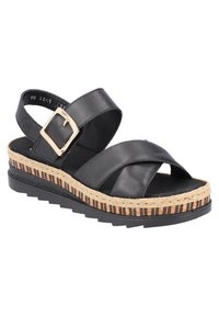 Sandale compensée en cuir noir avec des sangles croisées et une boucle dorée. Dispose d'une plateforme en jute tressé avec une texture rayée et une semelle noire.