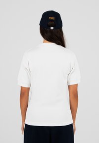 Biała, żeberkowana koszulka z krótkim rękawem o miękkiej fakturze, paired z ciemnoniebieską czapką z haftem "MODERN YUPPIES" w kolorze pomarańczowym.