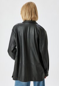 Schwarze Lederjacke mit entspannter Passform, geschichtetem Design und knöpfbaren Manschetten. Glatte Textur, klassischer Kragen und flache Nähte.